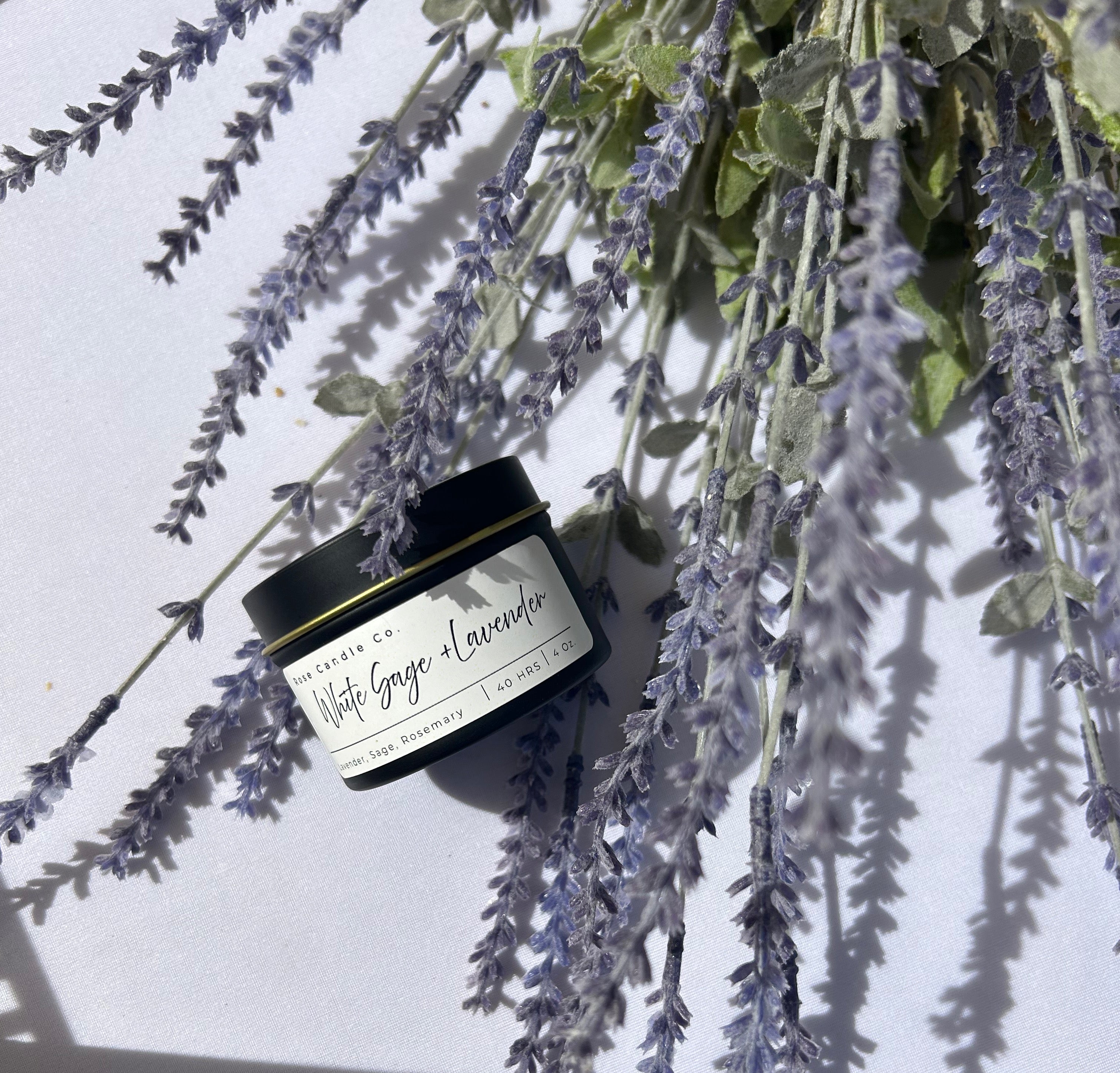 a gold lined black matte travel candle of White Sage & Lavender lying on a bed of lavender buds