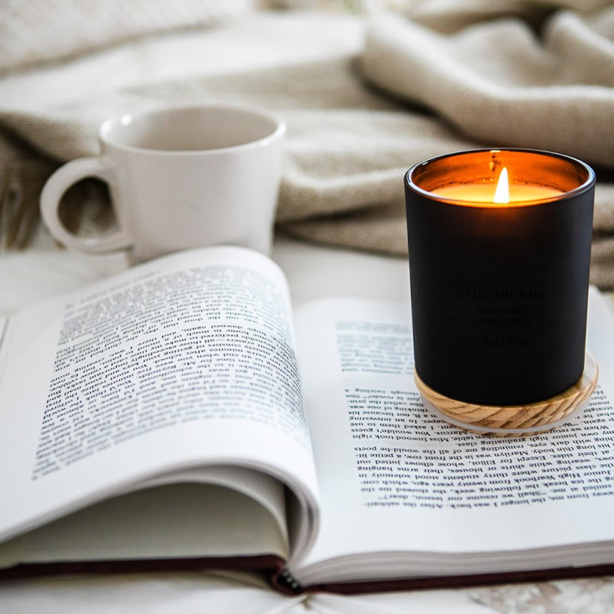black matte lighted candle w bamboo lid sitting on a couch with a blanket and coffee cup